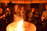 Young people are enjoying themselves around the open fire; talking and singing together with a Guitar